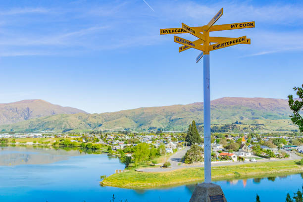 View of Cromwell from Luggate - Cromwell Road View of Cromwell from Luggate - Cromwell Road scenic outlook of township and blue lake with signpost pointing to New Zealand locations. alexandra township photos stock pictures, royalty-free photos & images