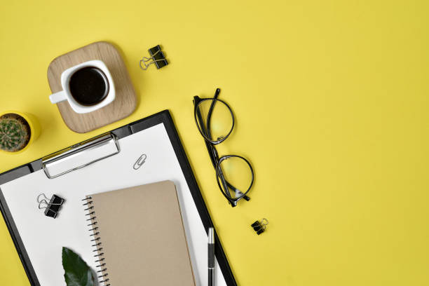 istock Office desk workspace with blank clip board, office supplies, pen, cactus, green leaf, coffee cup on a wooden stand and eye glasses on yellow background. Flat lay, top view blog concept 1136022039