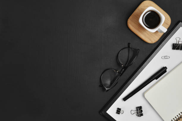 istock Mock up workspace with blank clip board, office supplies, pen, coffee cup, notepad and eyeglasses on dark background. Flat lay, top view, copy space 1136023012