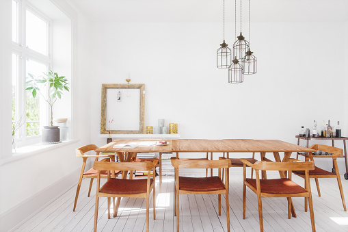 Stylish white dining table with wooden chairs in elegant dining room with art and decorations open to modern kitchen