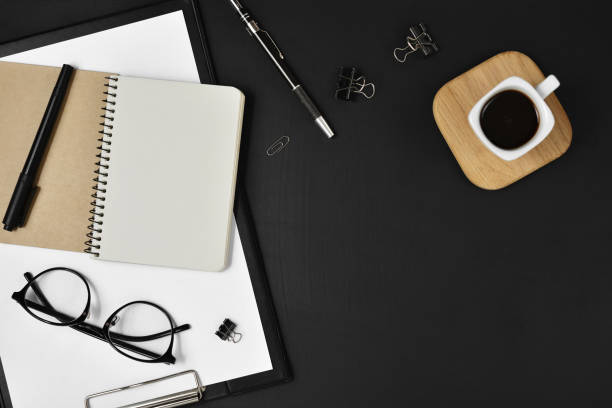 istock Flat lay, top view office table desk. Workspace with blank clip board, office supplies, pen, notepad, coffee cup on a wooden stand and eye glasses on black background. Blog concept 1136023610
