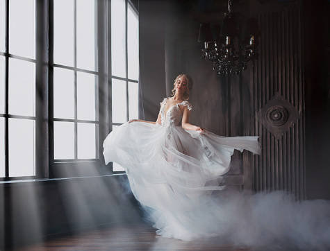 sweet and gentle girl with fair skin and blond hair dances alone in silence in an old castle, spirit of abandoned medieval building whirls in white smoke and magical thick fog in rays of sun.