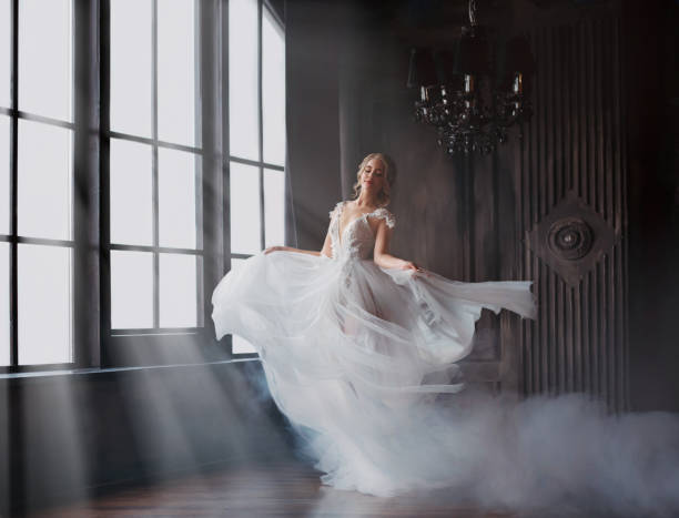 sweet and gentle girl with fair skin and blond hair dances alone in silence in an old castle, spirit of abandoned medieval building whirls in white smoke and magical thick fog in rays of sun - bride wedding fashion evening gown imagens e fotografias de stock