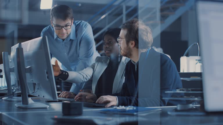 Two Electronics Development Engineers Working on Computers, Talk with Project Manager. Team of Professionals Use CAD Software for the Modern Industrial Engineering Design. Slow Motion