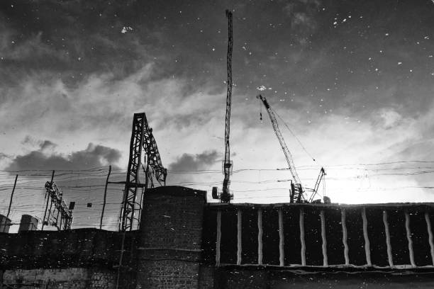 A reflection of cranes over a railway line near Kings Cross where the cranes are silhouetted in a rain puddle.
