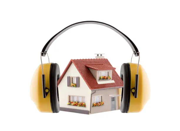 Photo of Protection against noise. Hearing protection yellow ear muffs with house miniature isolated on white background