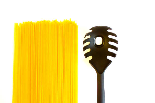 Long raw yellow spaghetti and black spoon with hole isolated on white background