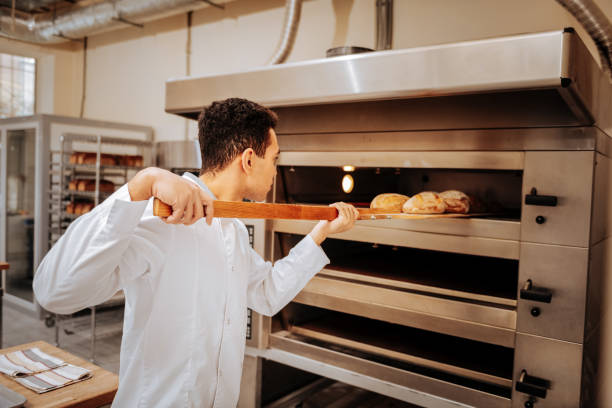 istock Young baker taking ready bread out of big oven in the kitchen 1136038084