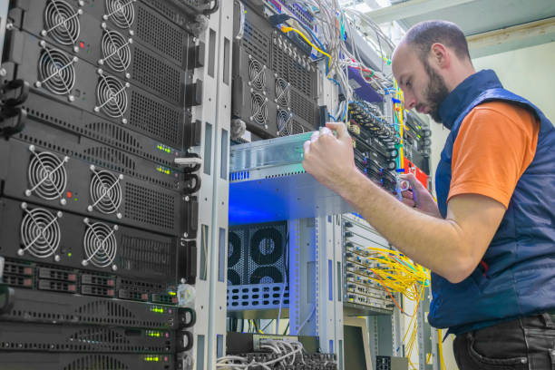 un homme travaille dans une salle de serveurs. l'administrateur système installe un nouveau serveur dans un centre de données moderne. un technicien répare le routeur central. - network server data center installing photos et images de collection