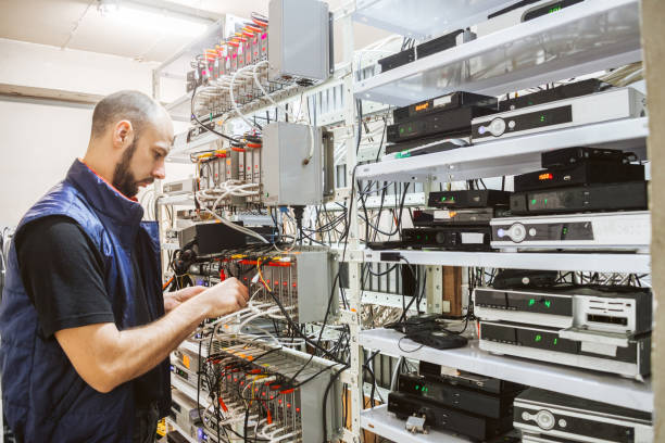 istock Worker works on the control panel in the data center. Specialist connects coaxial television wires in the rack of the TV station server room. Man switches  audio and video cable on the patch panel. 1136043206
