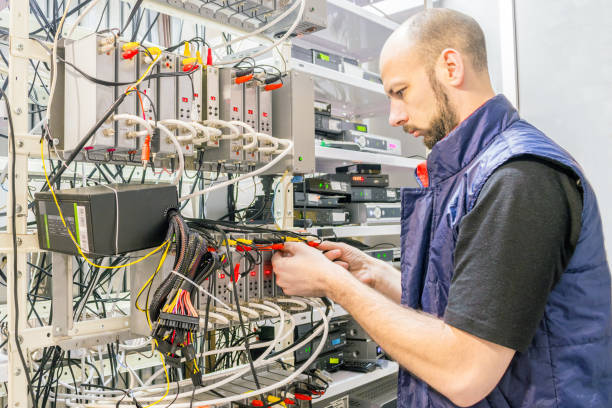 istock Man switches  audio and video cable on the patch panel. Worker works on the control panel in the data center. Specialist connects coaxial television wires in the rack of the TV station server room. 1136043211