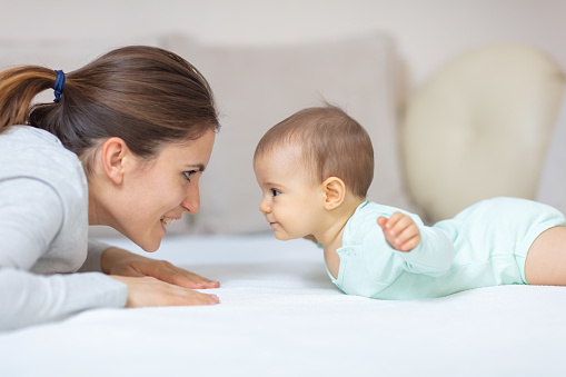 Mother and 7 months old baby doing exercises on the bed and learning to crawl