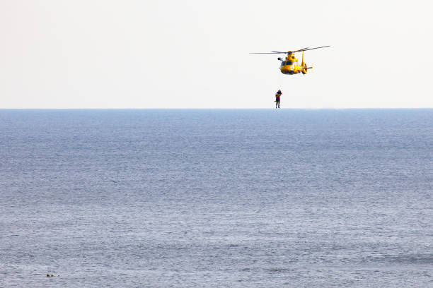 un helicóptero está rappel dos hombres sobre el mar - rescue helicopter coast guard protection fotografías e imágenes de stock