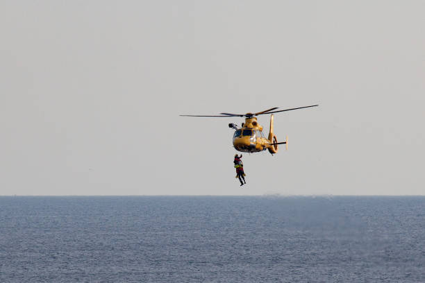 un helicóptero está rappel dos hombres sobre el mar - rescue helicopter coast guard protection fotografías e imágenes de stock