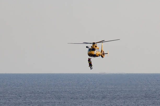 вертолет abseiling двух мужчин над морем - rescue helicopter coast guard protection стоковые фото и изображения