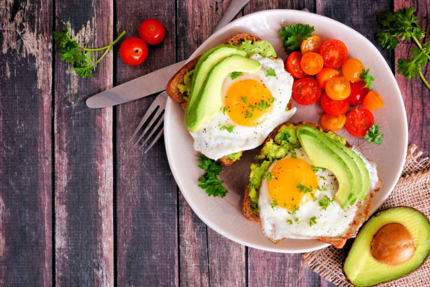 istock Avocado toasts with eggs and tomatoes, top view corner border against dark wood 1136048892
