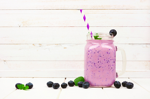 Healthy blueberry smoothie in a mason jar glass with scattered fruit over a white wood background