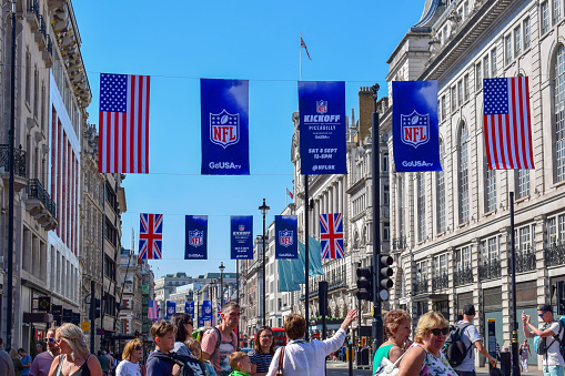 View of London street close to Picadilly Circus with American football banners, USA and UK flags, double-docker buses and tourists. Photo taken on a sunny summer day.