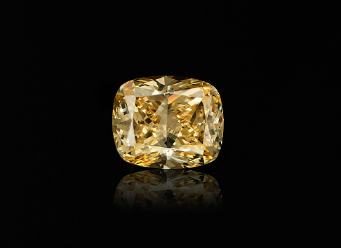 Yellow diamond on black background. Big faceted gem. Frontal view
