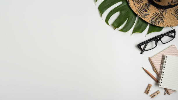 istock Flat lay, top view workspace with eye glasses, notebook, hat, pencil, green leaf, shoes and coffee cup on white background. Summer stylish traveller blogger concept. 1136057326