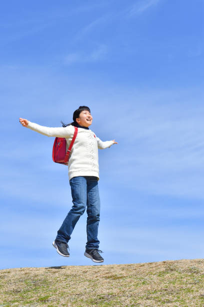 istock Japanese elementary school girl jumping in the blue sky 1136060057