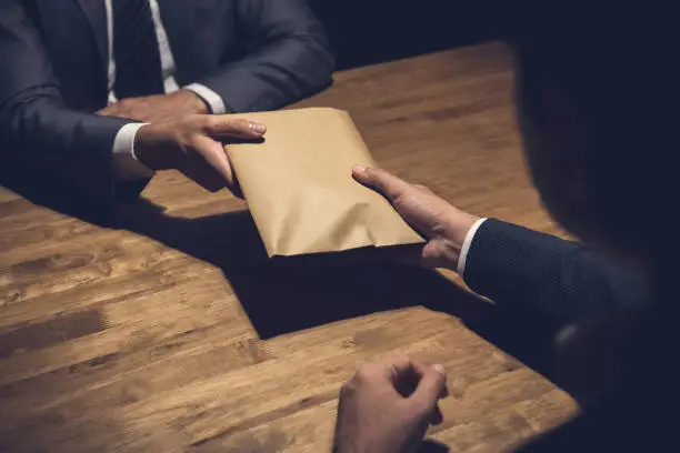Photo of Businessman giving money in the envelope to his partner in the dark