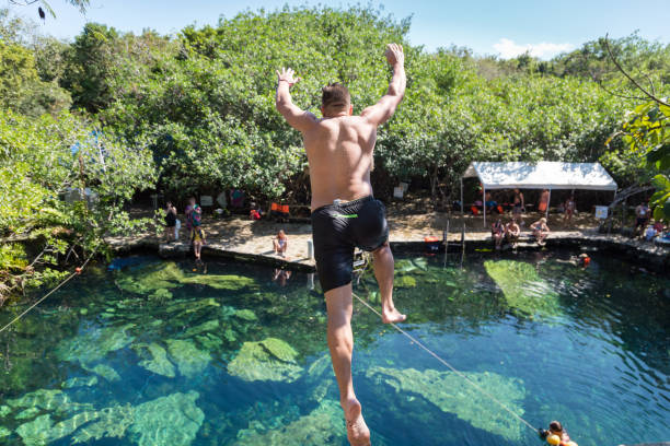 Man jumps off a cliff into the Cristalino cenote in Mexico. Man jumps off a cliff into the Cristalino cenote in Mexico cliff jumping stock pictures, royalty-free photos & images