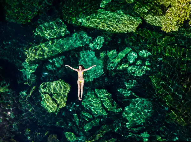 Overhead shot of a attractive young brunette woman in a bikini floating in the Cristalino cenote near Tulum, Mexico
