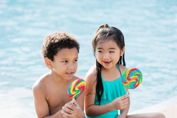 istock Two multi-ethnic children sitting by pool with lollipops 1136075403