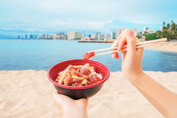 une fille mangeant et appréciant hawaiian ahi poke bowl sur waikiki beach - hawaiian food photos et images de collection