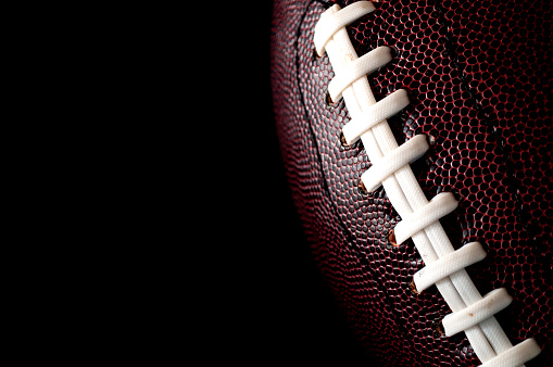 American football  and gameday poster concept with close up on the texture of a ball with dramatic moody light with high contrast and copy space on a dark black background