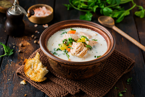 Warm Finnish creamy soup with salmon and vegetables in old ceramic bowl on old wooden background. Rustic style.
