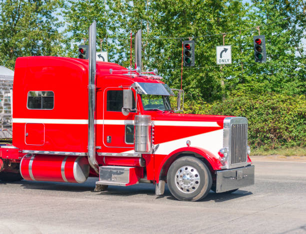 istock Bright red big rig classic American bonnet semi truck driving on intersection with traffic light 1136099310