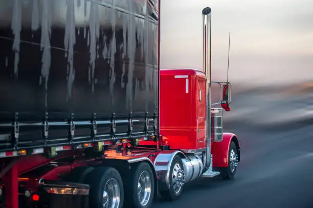 Photo of Bright red big rig semi truck with covered semi trailer going on the road for delivery