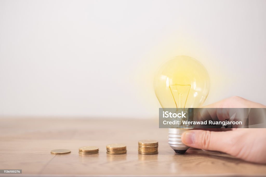 new idea concept with coins stack, young women hand holding light bulb with new knowledge on wooden backgrounds and new idea concept save power to save the earth Fuel and Power Generation Stock Photo