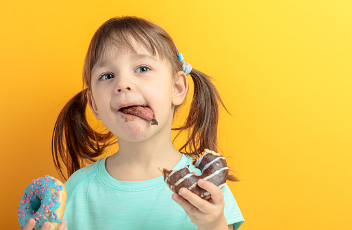 Girl in a turquoise shirt eat donuts.Yellow background. Copy space.