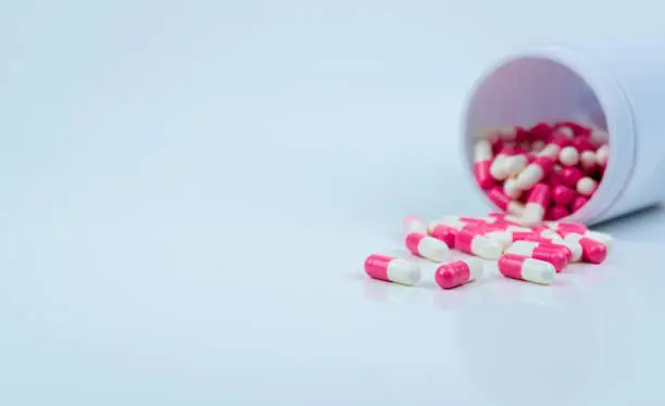 Pink-white capsule pills spread out of drug bottle. Antipsychotic drug. Capsule medicine for treatment depression. Anti-anxiety drug. Global healthcare. Pharmacy background. Pharmaceutical industry.