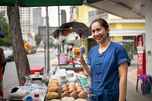 Asian Woman buying lunch from a street food vendor's cart in Chinatown in Bangkok, Thailand.