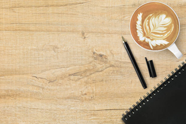 istock Wood office desk table with cup of latte coffee, notebook and pen. Top view with copy space, flat lay. 1136118325