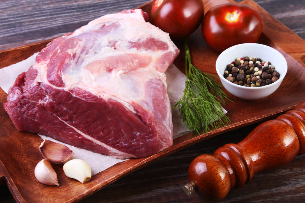 istock Raw pork steaks on wooden board with herbs, spices, tomatoes and pepper grinder ready for cooking. Selective focus 1136129954