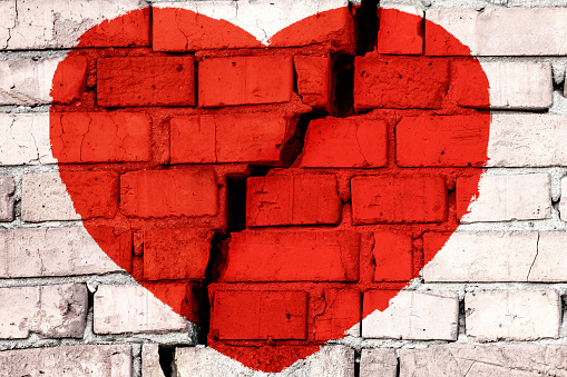 Red broken heart on the brick wall with big crack in the middle. Concept of broken love.