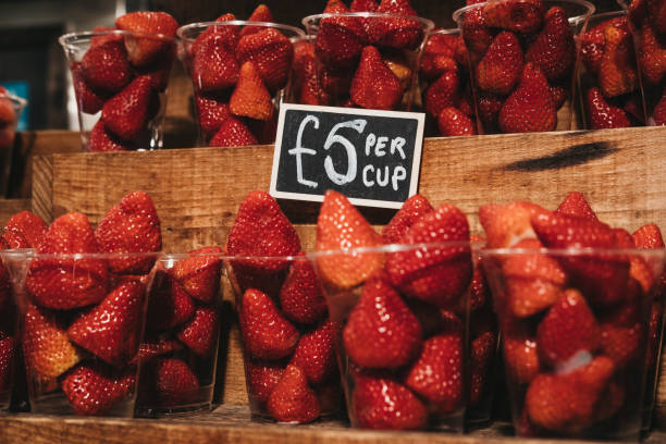 Cups of fresh strawberries on sale, portioned in plastic cups, on top of a wooden shelves.