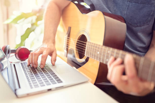 Musician playing acoustic guitar and recording music on computer Musician playing acoustic guitar and recording music on computer or learning fom online lesson chord photos stock pictures, royalty-free photos & images