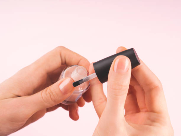 Applying nude nail polish to woman's hand Applying nude nail polish to woman's hand over delicate pink background. Close up. paint nail stock pictures, royalty-free photos & images