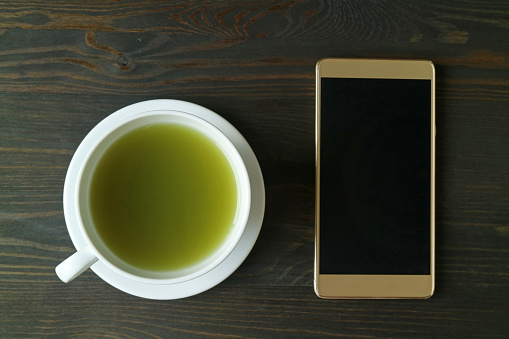 Top View of Hot Matcha Green Tea with an Empty Screen Smartphone on Dark Brown Wooden Table