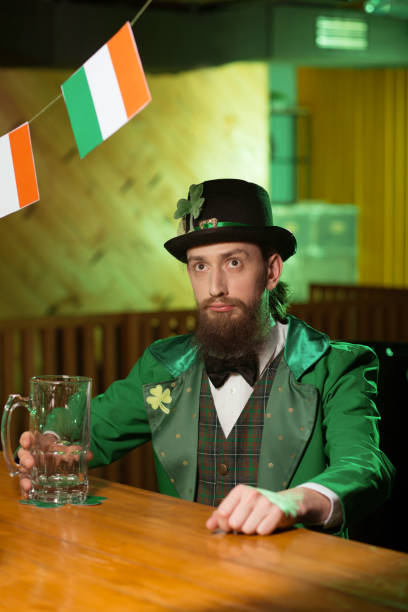 istock Dark-haired bearded young man in a leprechaun costume looking serious 1136151778