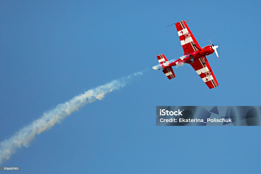 Red and white airplane with the trace of white smoke behind it in the sky in the airshow Airshow Stock Photo