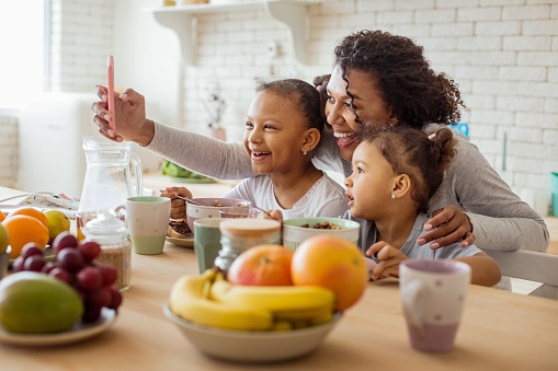 Look at us. Cheerful dark-skinned woman standing near her daughters while taking selfie photo