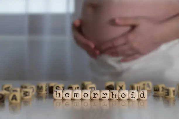 Word HEMORRHOID composed of wooden letters. Pregnant woman in the background