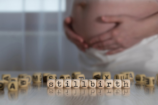 Word STILLBIRTH composed of wooden letters. Pregnant woman in the background